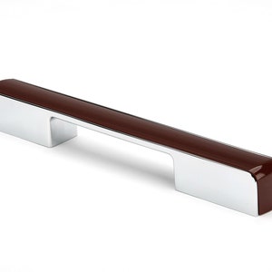 Peut inclure: Une poignée de tiroir en chrome avec un insert rectangulaire brun. La poignée a une forme rectangulaire arrondie.