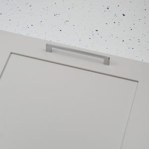 Pode incluir: Uma porta de armário cinza claro com uma puxador retangular prateado. O puxador está centralizado horizontalmente. O fundo é uma superfície branca com manchas azuis.