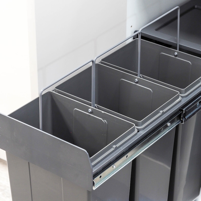 Pu&ograve; includere: Quattro bidoni della spazzatura grigi estraibili con maniglie in metallo, montati in un armadio da cucina.