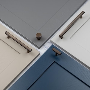 May include: An assortment of cabinet doors in various colors, including gray, beige, white, and navy blue. Each door features a different style of bronze-toned hardware, such as knobs and bar pulls, showcasing a range of design options for home decor.