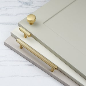 May include: Three gold cabinet knobs and pulls with a ribbed design. The knobs and pulls are displayed on a light gray surface.