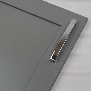 Peut inclure: Gros plan sur une porte d'armoire grise avec une poignée rectangulaire argentée. La poignée est montée horizontalement et a un design incurvé. La porte de l'armoire est de couleur grise unie.