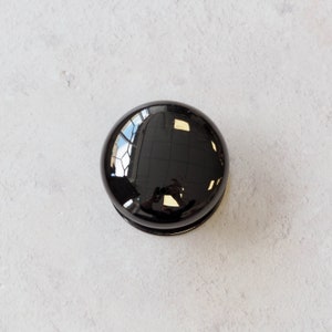 May include: A black round knob with a shiny, reflective surface.