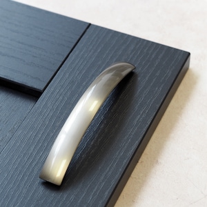 Puede incluir: Una manija de puerta de armario de plata con un diseño curvo. La manija está montada en una puerta de armario de madera gris oscuro.