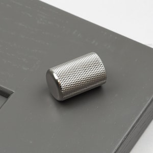 Può includere: Un pomello per armadio in metallo argentato con un motivo a rombi testurizzato.