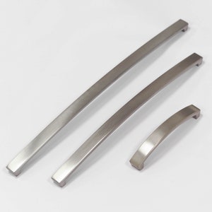 May include: Three silver metal cabinet door handles of different sizes. The handles are all curved and have a brushed finish.