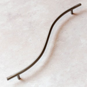 May include: A silver-toned, curved cabinet pull with a smooth, rounded design. The pull is approximately 10 inches long.