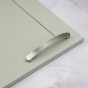 Könnte beinhalten: Ein gebürsteter Nickel-Schrankgriff mit gebogenem Design. Der Griff ist an einer hellgrünen Schranktür montiert.