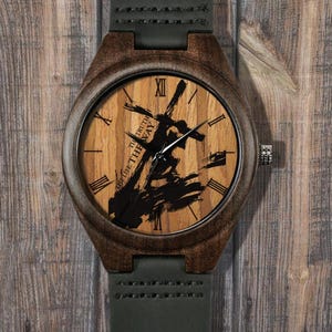 May include: Wooden wristwatch with a light brown face and dark brown frame. The watch face features a black abstract design and Roman numerals. The watch has a dark green leather strap and a silver crown. The text on the watch face reads "THE TRUTH THE WAY OF LIFE".