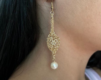 Peut inclure: Boucles d'oreilles pendantes dorées avec un design délicat et complexe et une seule perle blanche.