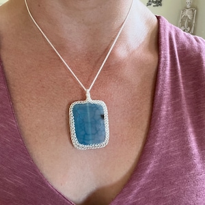 May include: A silver chain necklace with a blue agate pendant. The pendant is set in a silver frame and has a delicate, intricate design.