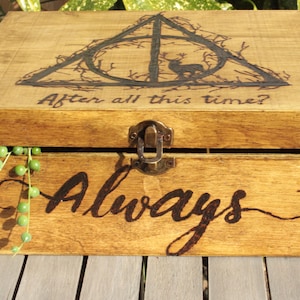 May include: Wooden box with a hinged lid and metal clasp. The lid features a burned design of a triangle with a deer and the text "After all this time?". The front of the box says "Always".