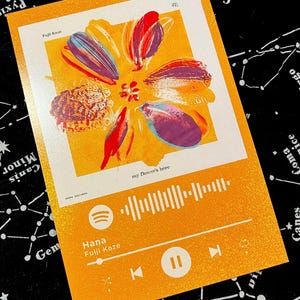 Op de afbeelding: Een oranje kunstafdruk met een gestileerd bloemdesign in rood, paars en geel. De afdruk bevat de tekst "Hana Fujii Kaze" en "my flower's here", plus een muziekspelerinterface.
