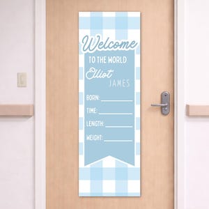 Könnte beinhalten: Ein blau-weiß kariertes Türschild mit dem Text "Willkommen auf der Welt" und Platz zum Eintragen des Babynamens, der Geburtsdaten, der Größe und des Gewichts. Das Schild hängt an einer hellbraunen Tür.