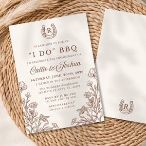 May include: Two cream-colored engagement announcement cards with brown text and floral illustrations. One card features the text "I DO" BBQ, names, and event details. The other card has a horseshoe logo. The cards rest on a woven mat.