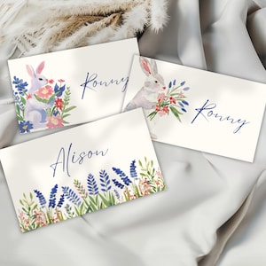 May include: Three watercolor place cards with floral and bunny illustrations. Two cards feature a bunny with flowers and the name "Ronny" in blue script. The third card has a floral border and the name "Alison".