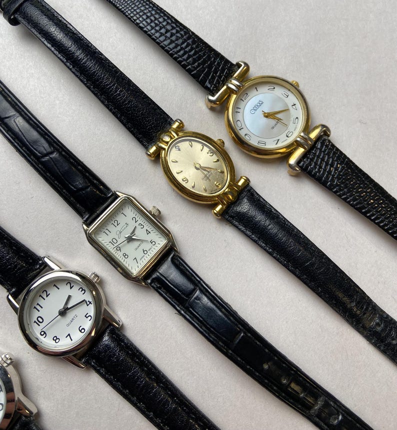 May include: Several vintage wristwatches with black leather bands and gold or silver-toned cases. The watch faces are white or gold, with Roman or Arabic numerals. Some watches have a rectangular or oval shape.