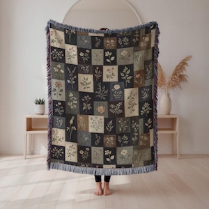 May include: A floral patterned throw blanket with a patchwork design. The blanket features squares with botanical illustrations in shades of cream, green, and brown. The edges are finished with a fringe in blue, red, and cream.