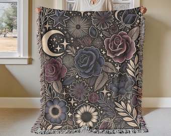 May include: A woven tapestry throw blanket with a dark background featuring a floral pattern with roses, stars, and a crescent moon. The design is in shades of purple, blue, and gold.