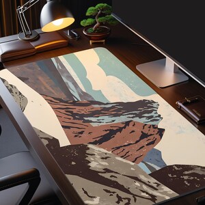 May include: A large rectangular desk mat featuring a landscape design with mountain and cloud illustrations in shades of brown, beige, blue, and gray. The mat is on a dark wooden desk, with a desk lamp, bonsai tree, and other office accessories.