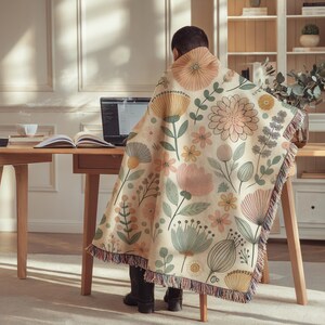 May include: A person sitting at a desk with a laptop and a floral patterned throw blanket draped over their shoulders. The blanket features a variety of flowers in shades of pink, yellow, and green.