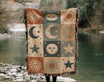 May include: A woven tapestry throw blanket with a patchwork design featuring suns, moons, and stars in shades of brown, orange, yellow, green, and blue.