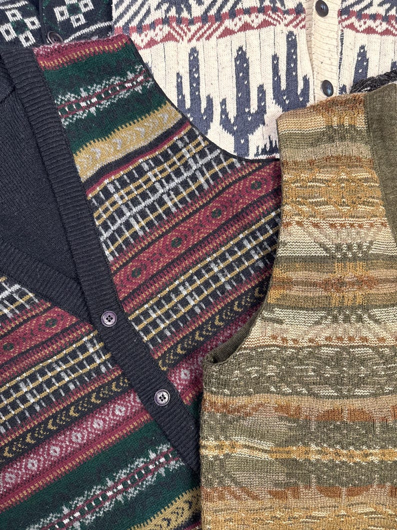 May include: Three different patterned knit vests. The first vest is black with a red, green, and gold geometric pattern. The second vest is cream with a red and white geometric pattern and a cactus design. The third vest is brown with a green, gold, and brown geometric pattern.