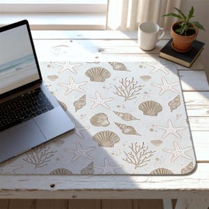 May include: A rectangular desk mat featuring a light blue background with a pattern of starfish, seashells, and coral in shades of beige and brown. A laptop is on the left side of the mat.