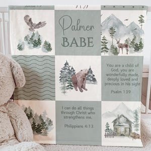 Könnte beinhalten: Eine Babydecke mit Patchwork-Design mit Waldtieren, Bergen und inspirierenden Zitaten. Die Decke hat ein salbeigrünes und weißes Farbschema, mit dem Aufdruck "Palmer BABE".
