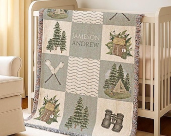 May include: A woven baby blanket with a camping theme. The blanket features squares with images of trees, a tent, binoculars, and crossed campfires. The name "JAMESON ANDREW" is printed on the blanket. The blanket is draped over a white crib.