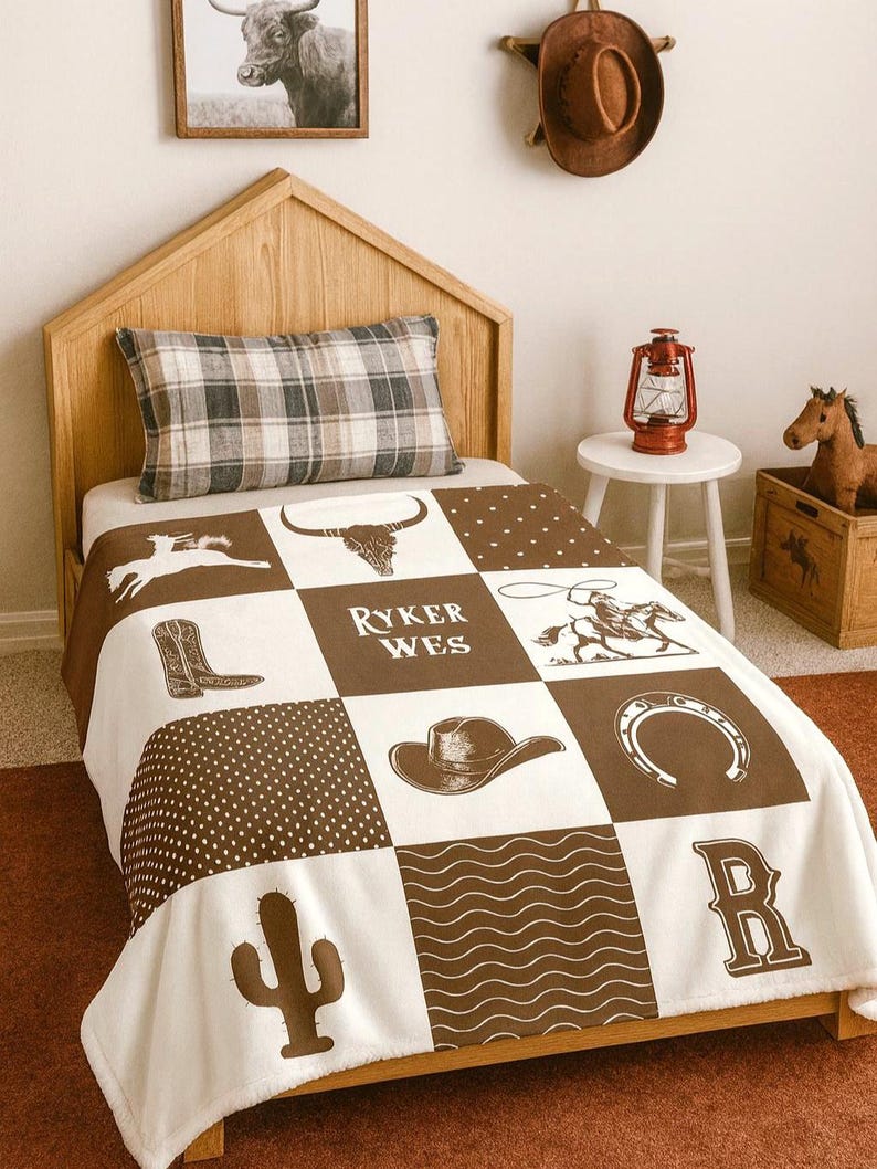 May include: A white and brown patchwork blanket featuring western-themed graphics including a bull skull, cowboy boots, a cowboy on a horse, a hat, a horseshoe, a cactus, and the text RYKER WES, arranged in a grid pattern with polka dot and wavy line squares.