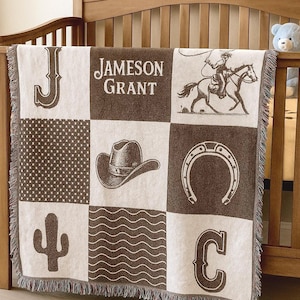 May include: A woven throw blanket featuring a grid of nine squares in brown and cream. The design includes the name Jameson Grant, the letters J and C, a cowboy on a horse, a cowboy hat, a horseshoe, a cactus, and geometric patterns.