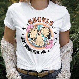 May include: White t-shirt with a graphic of three ghosts in a rainbow circle. The text "Ghouls Just Wanna Have Fun" is written around the circle.