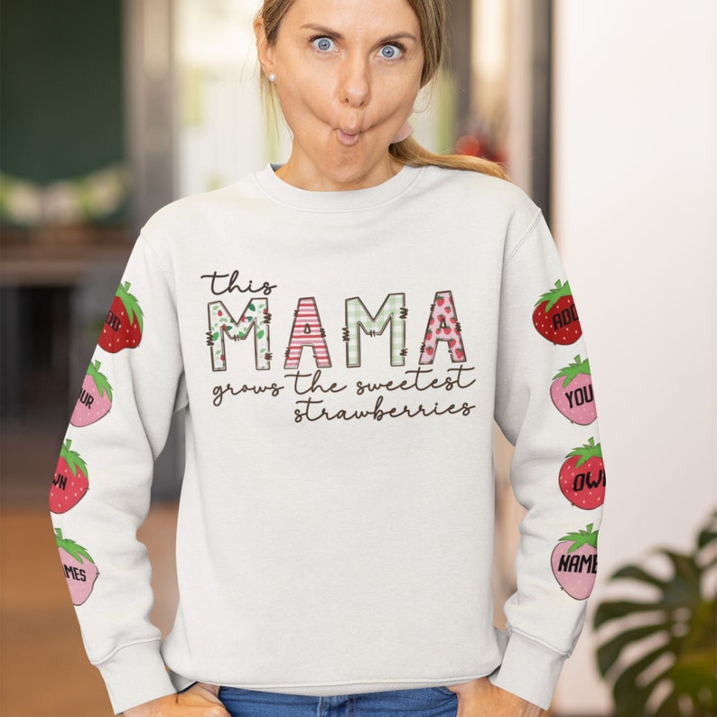 May include: White sweatshirt with the text "This Mama grows the sweetest strawberries" and a patchwork design of the word "Mama". The sleeves have a pattern of strawberries with names on them.