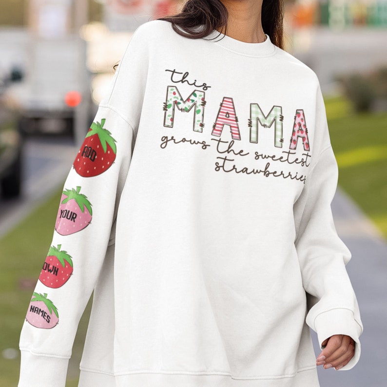 May include: White sweatshirt with the text "This Mama grows the sweetest strawberries" and a patchwork design of the word "Mama" with strawberries on the sleeves.