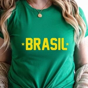 Puede incluir: Camiseta verde con la palabra "BRASIL" en letras amarillas y una estrella amarilla a cada lado de la palabra.