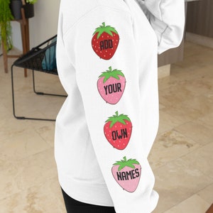 May include: White hoodie with a red and pink strawberry design on the sleeve. The strawberries have the words "ADD YOUR OWN NAMES" written on them.