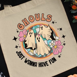 May include: A white tote bag with a colorful graphic of three ghosts and flowers. The text "Ghouls Just Wanna Have Fun" is printed in black on the bag.