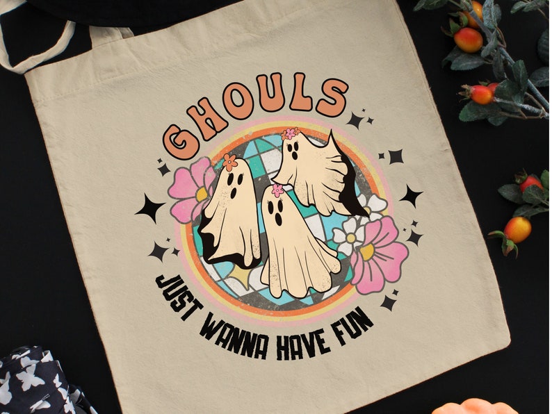 May include: A white tote bag with a colorful graphic of three ghosts and flowers. The text "Ghouls Just Wanna Have Fun" is printed in black on the bag.