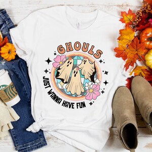 May include: White t-shirt with a retro-style graphic of three ghosts in a circle with the text "Ghouls Just Wanna Have Fun".