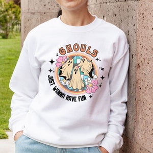 May include: White sweatshirt with a colorful graphic of ghosts and flowers. The text "Ghouls Just Wanna Have Fun" is printed on the sweatshirt.