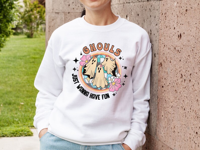 May include: White sweatshirt with a colorful graphic of ghosts and flowers. The text "Ghouls Just Wanna Have Fun" is printed on the sweatshirt.