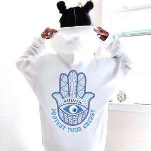 May include: White hoodie with a blue Hamsa hand design on the back, featuring an eye symbol and the text "Protect Your Energy". The design is in shades of blue and white.