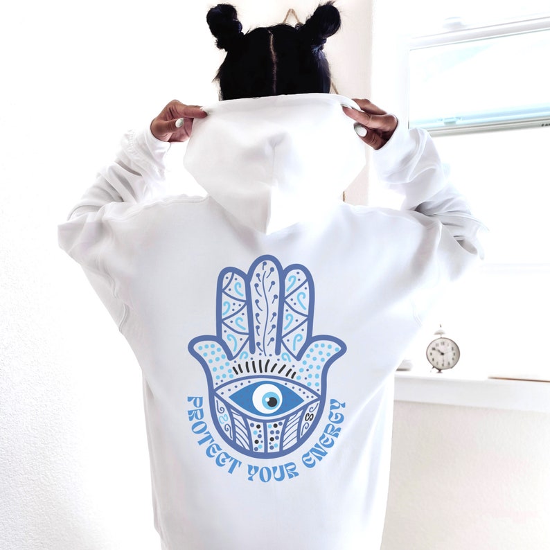 May include: White hoodie with a blue Hamsa hand design on the back, featuring an eye symbol and the text "Protect Your Energy". The design is in shades of blue and white.