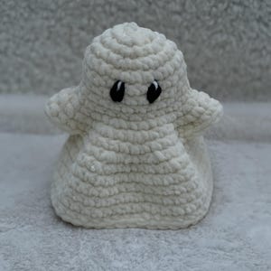 Peut inclure: Une petite figurine de fantôme crochetée en blanc, fabriquée à partir d'un fil pelucheux et doux. Le fantôme présente une tête arrondie, deux petits bras s'étendant sur les côtés et une base large et arrondie. Il a deux yeux ovales noirs brodés.