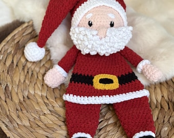May include: A handmade crochet Santa Claus doll. The doll is dressed in a red suit with a black belt and yellow buckle. The hat and beard are white. The doll is sitting on a woven basket.