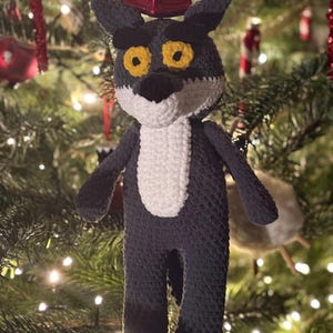 Puede incluir: Adorno de lobo de ganchillo hecho a mano, con pecho blanco y ojos amarillos, colgado de un árbol de Navidad. El lobo es gris oscuro con pecho blanco. Un adorno caprichoso para la decoración navideña.