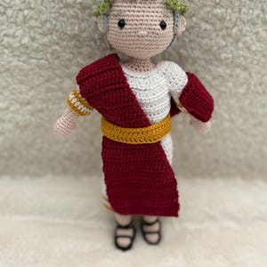 Peut inclure: Poupée crochetée représentant un empereur romain. La poupée porte une tunique blanche, une toge rouge et une ceinture dorée. Elle a des cheveux gris, une couronne de laurier et des sandales noires. La poupée est faite à la main.