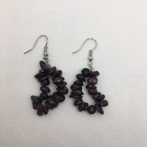 Puede incluir: Un par de pendientes colgantes con un gancho plateado y un racimo de cuentas de piedras preciosas de color rojo oscuro.