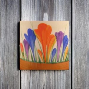 May include: A close-up of a ceramic tile featuring a painted design of orange, blue and purple crocuses. The flowers are arranged in a cluster and have a stylised, abstract look.